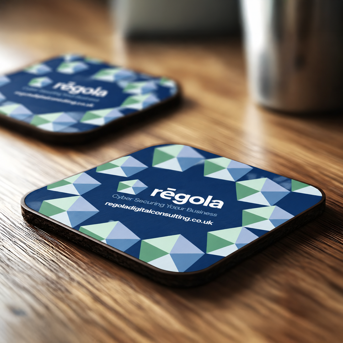 Regola branded coasters featuring the new logo and a blue, green and white geometric pattern.