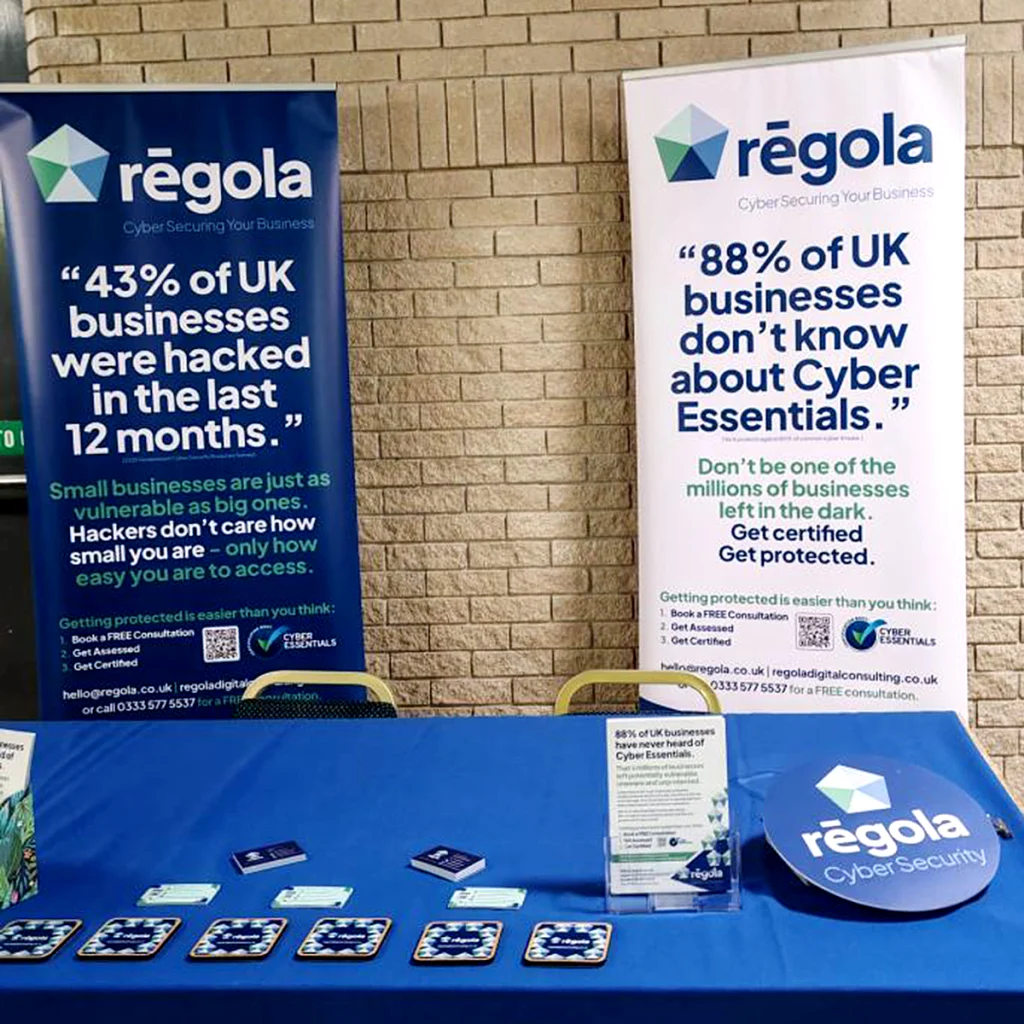 Regola event display with two roll-up banners, printed leaflets and branded coasters arranged on a blue tablecloth.