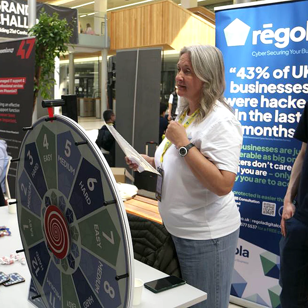 Exhibition visitor taking part in Regola’s cyber security spinning wheel activity beside a branded banner.