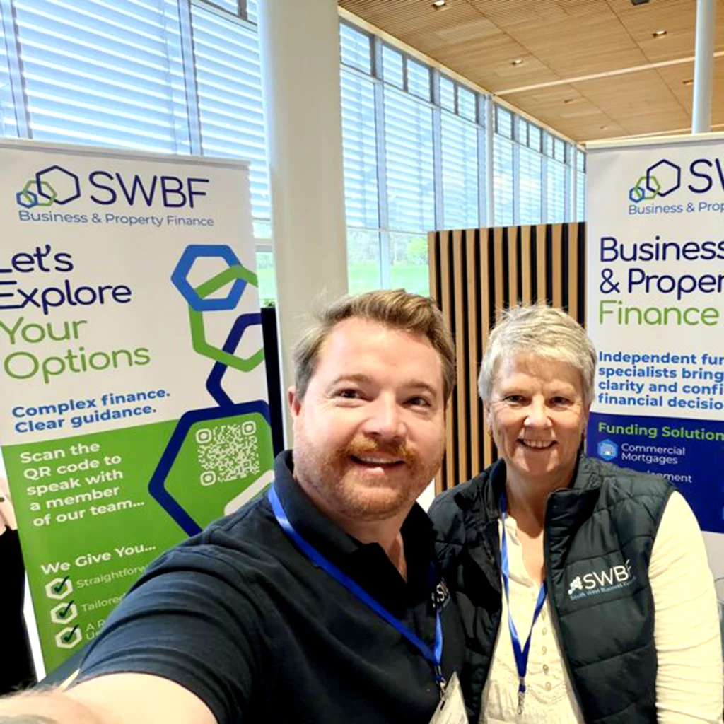 Two SWBF team members standing in front of branded roller banners at an event